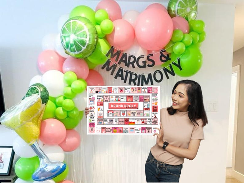 May include: A pink and green balloon arch with the text "MARGS & MATRIMONY" in black letters. A person is holding a game board with the text "DRUNKOPOLY" in red letters.