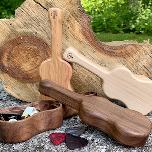 Peut inclure: Objets en bois en forme de guitare de différentes teintes, dont marron clair, moyen et foncé. Une petite boîte en bois et des médiators sont également présents. Les objets en forme de guitare ont un logo d'arbre sur la tête.
