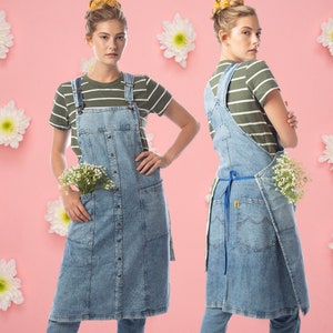May include: Two people wearing denim overalls with a striped shirt underneath. Both are holding small bouquets of white flowers. The background is a light pink with white flowers.