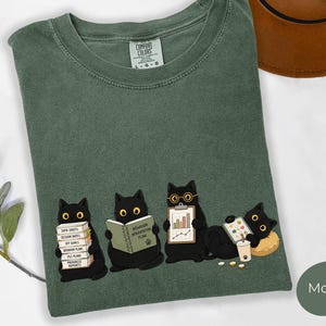Puede incluir: Una camiseta verde musgo con un gráfico de cuatro gatos negros. Uno sostiene una pila de papeles con los textos Data Sheets, Session Notes, IEP Goals, Behavior Plans y Progress Reports. Otro sostiene un libro Behavior Intervention Plan.