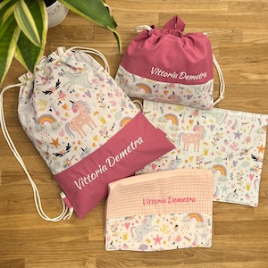 Può includere: Un set di articoli in tessuto che include un grande zaino con coulisse, una piccola sacca con coulisse, una pochette rettangolare piatta e una pochette con trama a nido d'ape. Ogni articolo presenta un motivo con unicorni, arcobaleni e stelle.