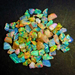 Puede incluir: Una colección de virutas de ópalo iridiscente en varios tonos de azul, verde, amarillo y naranja. Las virutas están esparcidas sobre una superficie negra.