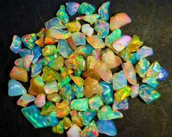 May include: A collection of iridescent opal chips in various shades of blue, green, yellow, and orange. The chips are scattered on a black surface.