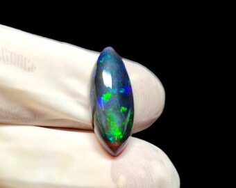 May include: A dark green, blue, and black oval-shaped black opal gemstone.