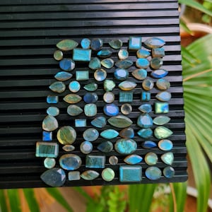 Puede incluir: Una colección de piedras preciosas de labradorita de diferentes formas y tamaños, en tonos azules y verdes. Las piedras preciosas están dispuestas sobre un fondo negro.