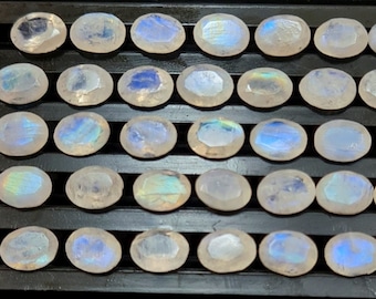 May include: A collection of 36 oval-shaped moonstone gemstones, each with a unique iridescent sheen. The stones are arranged in rows on a black surface.