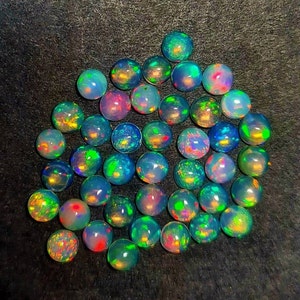 May include: A collection of iridescent opal gemstones in various shades of green, blue, and purple. The gemstones are round and have a smooth, polished finish.