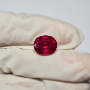 May include: A deep red oval-shaped gemstone with facets.