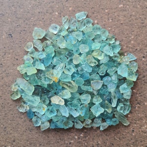 May include: A large pile of light blue aquamarine gemstone chips. The chips are irregular in shape and size, with some having a slightly yellow hue.