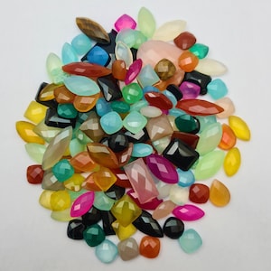 Puede incluir: Un gran surtido de cabujones de piedras preciosas de colores en varias formas y tama&ntilde;os. Los cabujones son una mezcla de verde, azul, rojo, naranja, amarillo, rosa y negro.