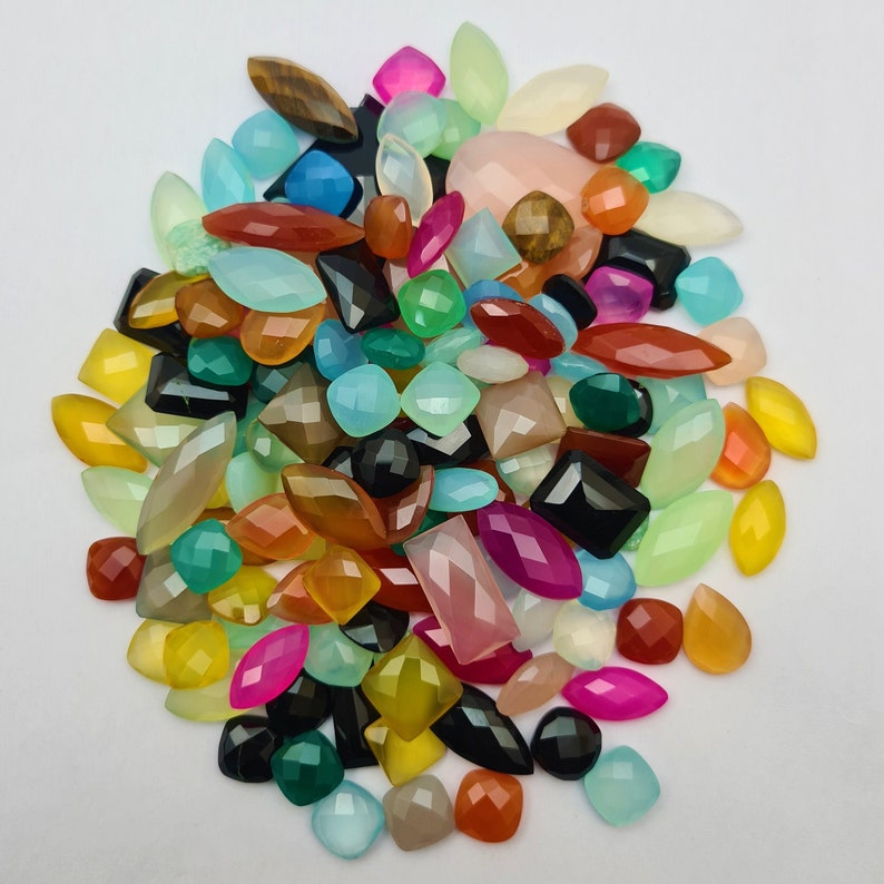Puede incluir: Un gran surtido de cabujones de piedras preciosas de colores en varias formas y tama&ntilde;os. Los cabujones son una mezcla de verde, azul, rojo, naranja, amarillo, rosa y negro.