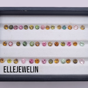 Könnte beinhalten: Ein schwarzes Tablett mit weißem Innenraum, das Reihen kleiner, runder, bunter Edelsteine enthält. Die Edelsteine sind in Reihen angeordnet und haben verschiedene Grüntöne, Rosa, Gelb und Braun. Der Text "ELLEJEWELIN" ist auf der Unterseite des Tabletts aufgedruckt.