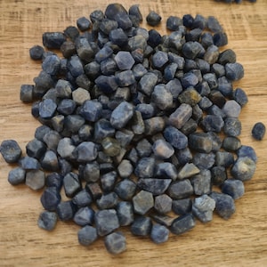 Peut inclure: Un grand tas de petits cristaux de saphir bleu foncé. Les cristaux sont bruts et présentent une variété de formes et de tailles.