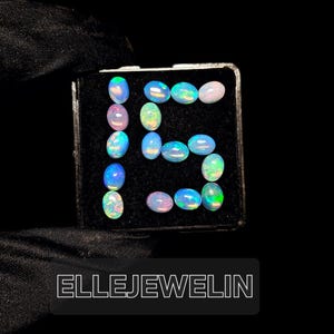 Könnte beinhalten: Eine schwarze Schachtel mit 15 ovalen Opalen in verschiedenen Blautönen, Grüntönen und Weiß. Die Opale sind in Form der Zahl "15" angeordnet.