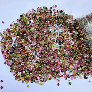 Op de afbeelding: Een grote stapel kleine, ronde, veelkleurige edelstenen. De edelstenen zijn een mix van groen, roze, rood en bruin.