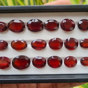 Puede incluir: Una colección de 15 piedras preciosas ovaladas de color rojo, presentadas en una caja de terciopelo negro con compartimentos blancos.