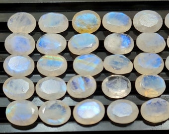May include: A collection of 20 oval-shaped moonstone cabochons. The stones are a milky white color with iridescent blue and green flashes.