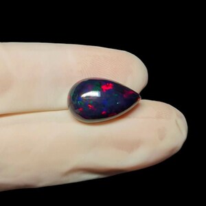 K&ouml;nnte beinhalten: Ein tropfenf&ouml;rmiger schwarzer Opal-Edelstein mit roten, gr&uuml;nen und blauen Schimmern.