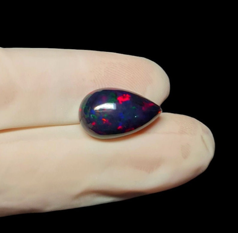K&ouml;nnte beinhalten: Ein tropfenf&ouml;rmiger schwarzer Opal-Edelstein mit roten, gr&uuml;nen und blauen Schimmern.