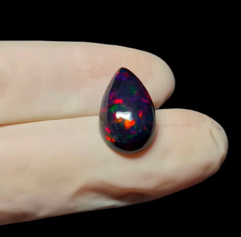 K&ouml;nnte beinhalten: Ein tropfenf&ouml;rmiger schwarzer Opal-Edelstein mit roten, gr&uuml;nen und blauen Schimmern.