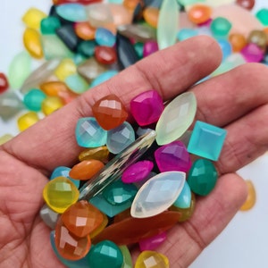 Puede incluir: Una variedad de cabujones de piedras preciosas de colores en diferentes formas y tama&ntilde;os, incluyendo ovalados, redondos, cuadrados y rectangulares. Las piedras preciosas son una mezcla de verde, azul, rosa, naranja, amarillo y blanco.