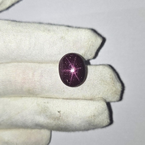 May include: A deep purple star ruby cabochon gemstone with a six-pointed star.