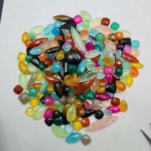 Puede incluir: Un gran surtido de cabujones de piedras preciosas de colores en varias formas y tama&ntilde;os. Los cabujones son una mezcla de piedras opacas y transl&uacute;cidas, incluyendo verde, azul, rosa, rojo, naranja, amarillo y marr&oacute;n.