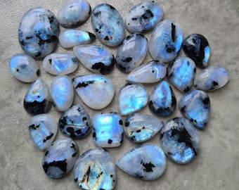 May include: A collection of iridescent rainbow moonstone cabochons with black inclusions. The stones are various shapes and sizes, and have a pearlescent sheen.