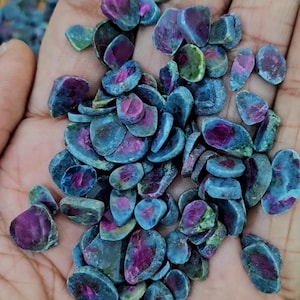 May include: A handful of raw gemstones with a mix of colors. The stones have a dark blue-green exterior with a vibrant magenta interior. The stones vary in size and shape, with a natural, organic appearance.
