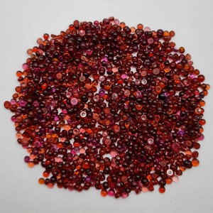 May include: A large pile of red and pink gemstone cabochons. The cabochons are round and have a smooth, polished surface.