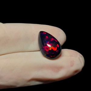 K&ouml;nnte beinhalten: Ein tropfenf&ouml;rmiger schwarzer Opal-Edelstein mit roten und gr&uuml;nen Farbschimmern.