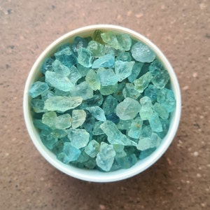 May include: A white bowl filled with light blue and green aquamarine crystals.