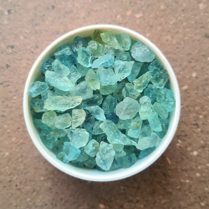 May include: A white bowl filled with light blue and green aquamarine crystals.
