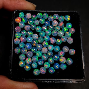 May include: A collection of round, iridescent opal gemstones in a black velvet box. The opals are various shades of blue, green, and pink.