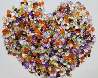 May include: A heart-shaped arrangement of colourful gemstones, including amethyst, citrine, peridot, and ruby. The stones are various sizes and shapes, creating a vibrant and textured display.