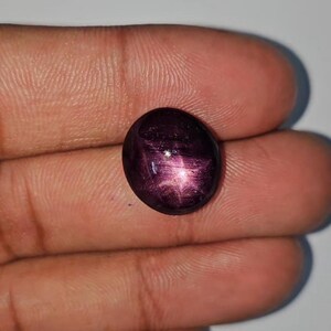 Könnte beinhalten: Ein dunkelvioletter, ovaler Edelstein mit Sterneneffekt. Die polierte Oberfläche reflektiert das Licht und erzeugt ein Sternmuster. Die tiefe Farbe entsteht durch Einschlüsse im Stein. Für Schmuck geeignet.