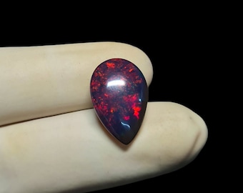 May include: A teardrop-shaped black opal gemstone with red and orange flashes of color.