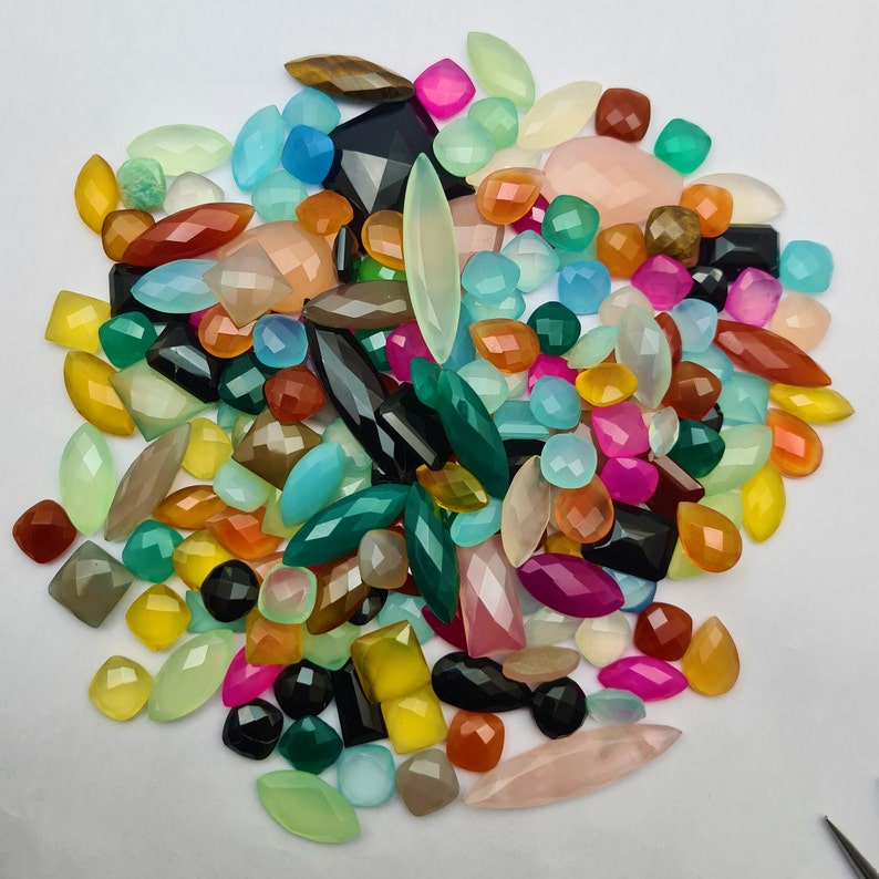 Puede incluir: Una gran colecci&oacute;n de cabujones de piedras preciosas de colores en varias formas y tama&ntilde;os. Los cabujones son una mezcla de verde, azul, rojo, naranja, amarillo, rosa y marr&oacute;n.