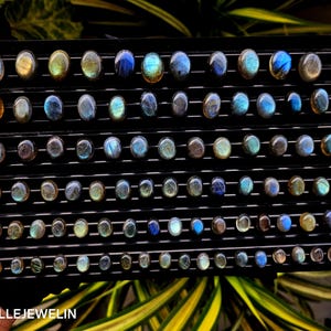 May include: A display of 60 round, iridescent labradorite gemstones in various shades of blue, green, and gold. The stones are arranged in rows on a black background.