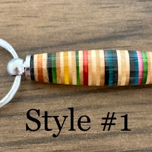 May include: A colorful, multi-striped wooden keychain with a silver key ring. The keychain is made from recycled skateboard wood. "Style #1" is printed below the keychain.