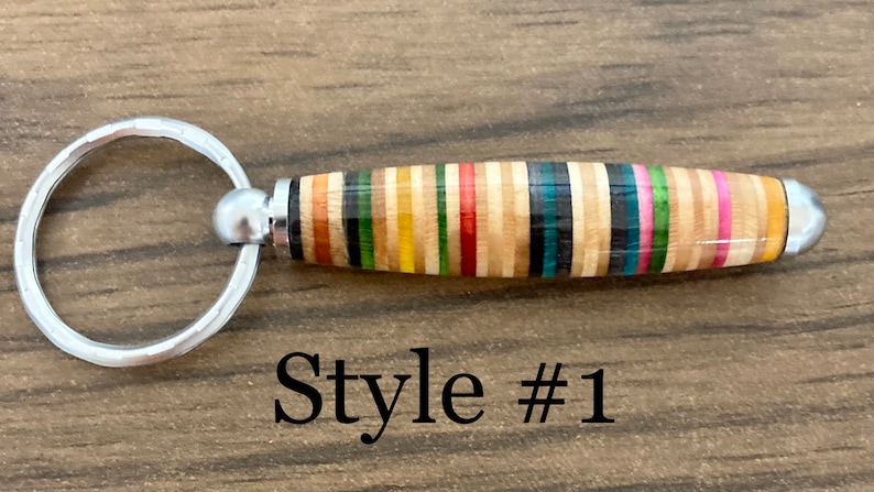 May include: A colorful, multi-striped wooden keychain with a silver key ring. The keychain is made from recycled skateboard wood. "Style #1" is printed below the keychain.