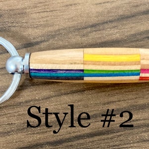 May include: A wooden keychain with a silver ring and a colorful wood inlay. The keychain has a rainbow stripe pattern and the text "Style #2" is visible below the keychain.