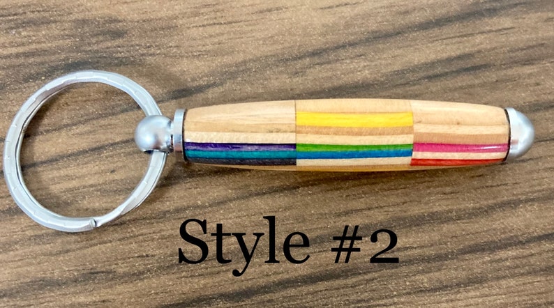 May include: A wooden keychain with a silver ring and a colorful wood inlay. The keychain has a rainbow stripe pattern and the text "Style #2" is visible below the keychain.
