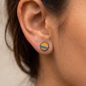 K&ouml;nnte beinhalten: Nahaufnahme eines Ohrs mit einem runden Ohrstecker. Der Ohrring hat ein gestreiftes Design in Blau, Orange und Gelb. Der Ohrring ist in einem silberfarbenen Metall gefasst. Der Ohrring hat eine kleine, kreisf&ouml;rmige Form.