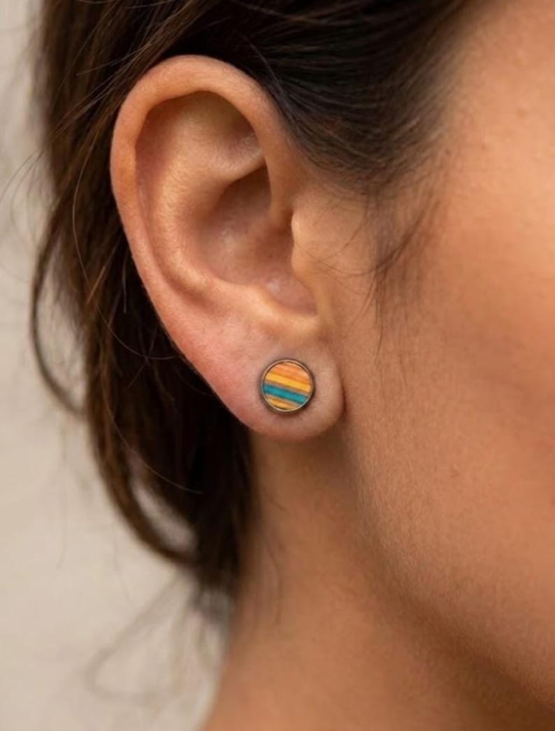 K&ouml;nnte beinhalten: Nahaufnahme eines Ohrs mit einem runden Ohrstecker. Der Ohrring hat ein gestreiftes Design in Blau, Orange und Gelb. Der Ohrring ist in einem silberfarbenen Metall gefasst. Der Ohrring hat eine kleine, kreisf&ouml;rmige Form.