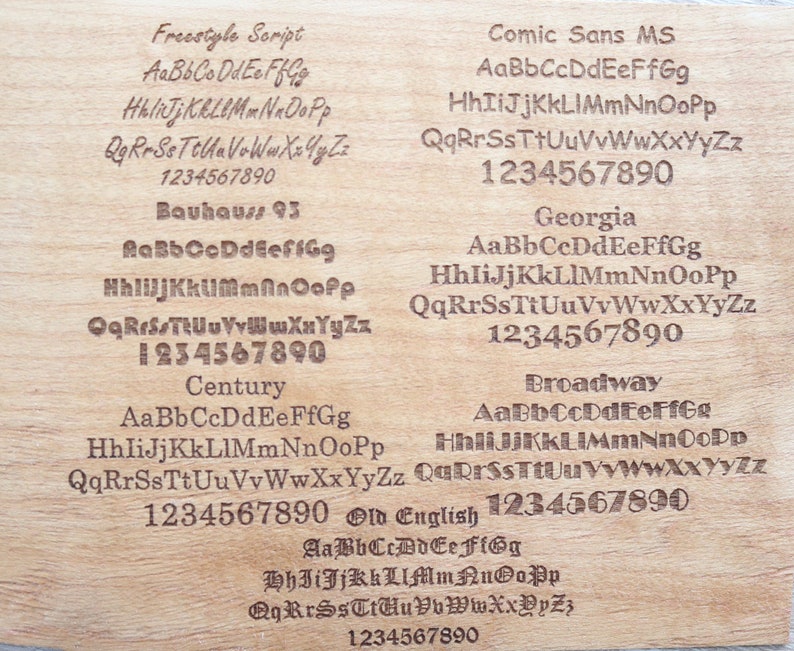 Puede incluir: Una superficie de madera clara muestra ejemplos grabados de varias fuentes, incluyendo Freestyle Script, Comic Sans MS, Bauhaus 93, Georgia, Century, Broadway y Old English. Cada fuente muestra el alfabeto y los n&uacute;meros.