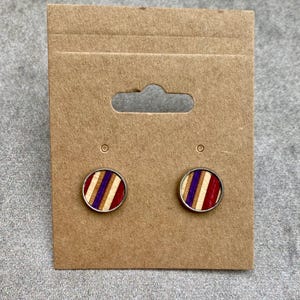 K&ouml;nnte beinhalten: Runde Ohrstecker mit silberfarbenem Rand. Die Ohrringe haben ein gestreiftes Design mit roten, lila und nat&uuml;rlichen Holzt&ouml;nen. Sie werden auf einer braunen Ohrringkarte aus Pappe pr&auml;sentiert.