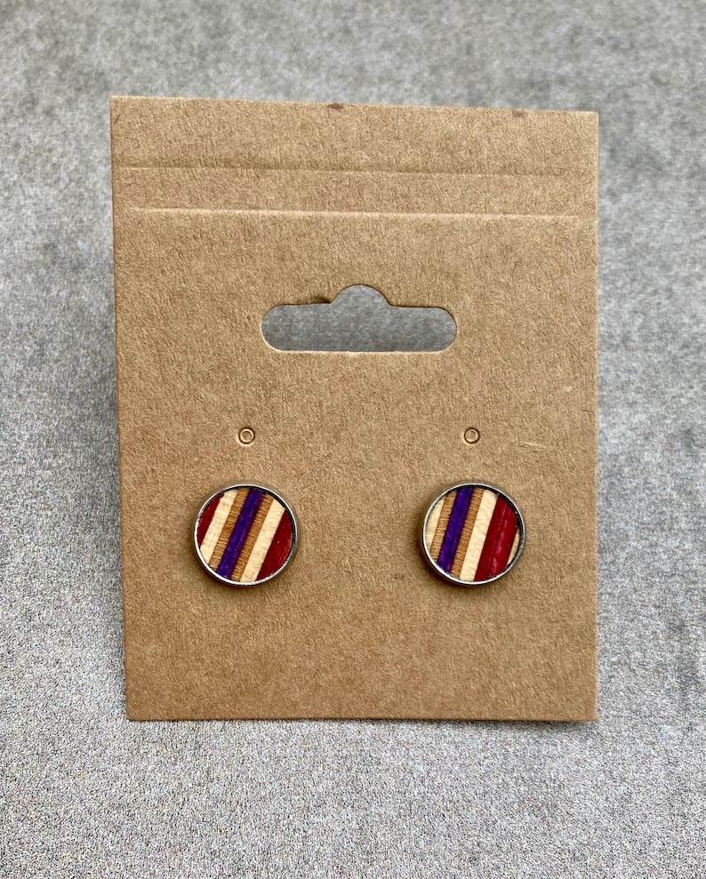 K&ouml;nnte beinhalten: Runde Ohrstecker mit silberfarbenem Rand. Die Ohrringe haben ein gestreiftes Design mit roten, lila und nat&uuml;rlichen Holzt&ouml;nen. Sie werden auf einer braunen Ohrringkarte aus Pappe pr&auml;sentiert.