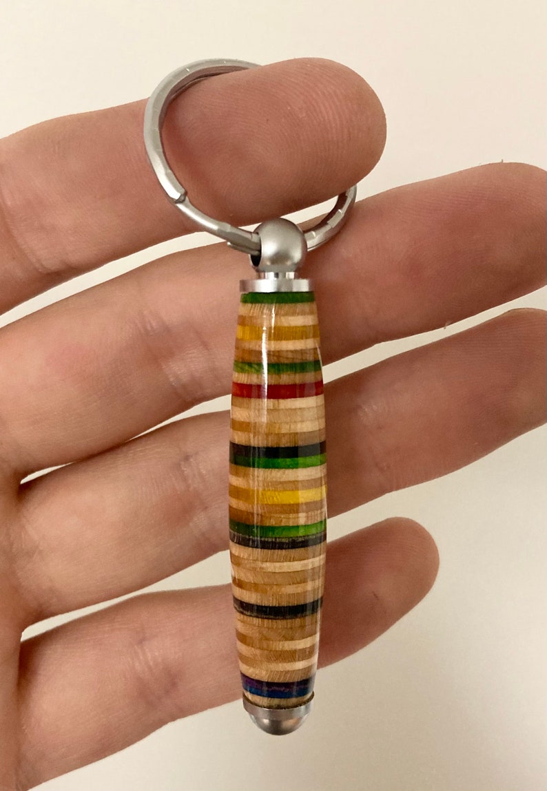 May include: A colorful wooden keychain with a silver key ring. The keychain is made from layered wood with stripes of red, yellow, green, and blue.