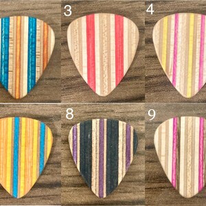 Puede incluir: Diez p&uacute;as de guitarra de madera con rayas verticales en varios colores, incluyendo azul, verde, naranja, rojo, morado y amarillo. Cada p&uacute;a tiene un patr&oacute;n de rayas &uacute;nico, mostrando una variedad de tonos de madera.